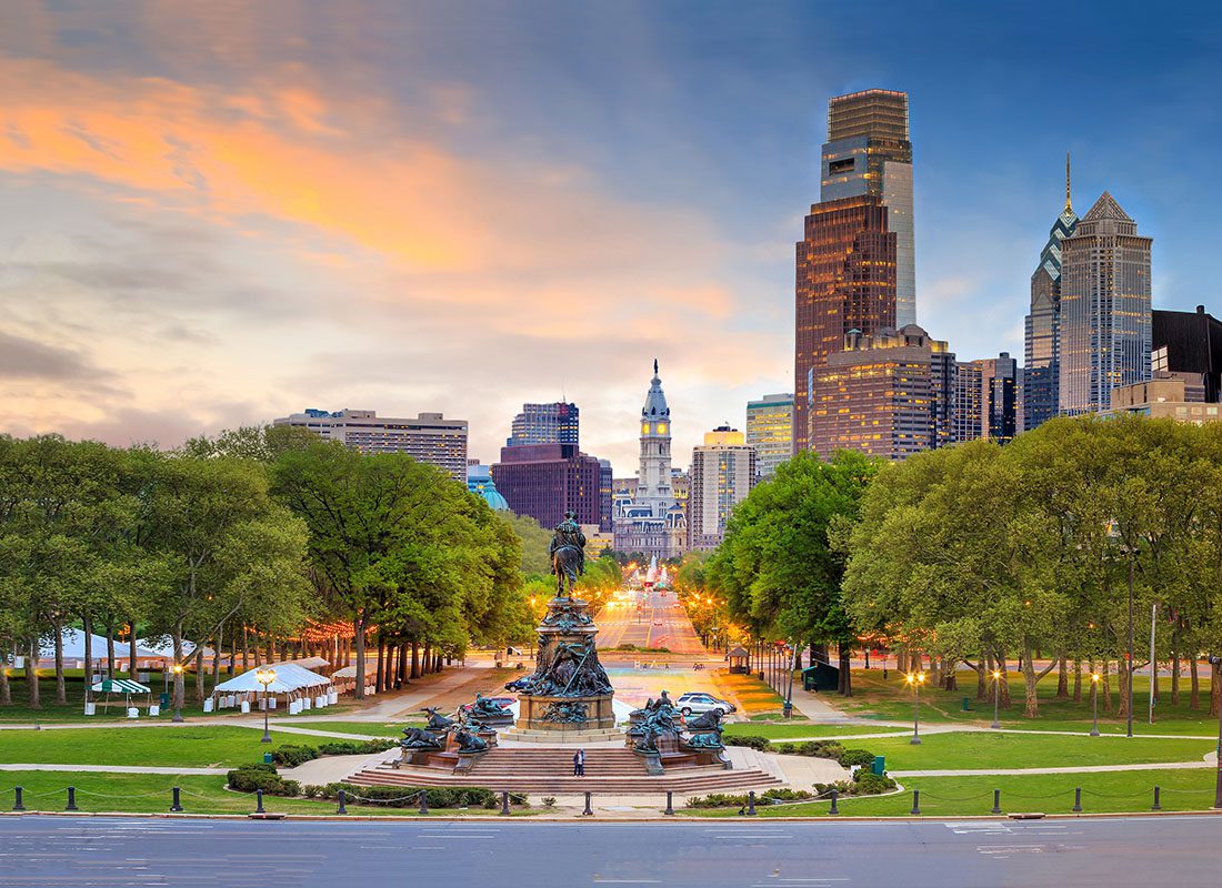 About Our Agency - View of a Statue at a Park with Green Trees in Downtown Philadelphia at Sunset with Views of Skyscrapers in the Background